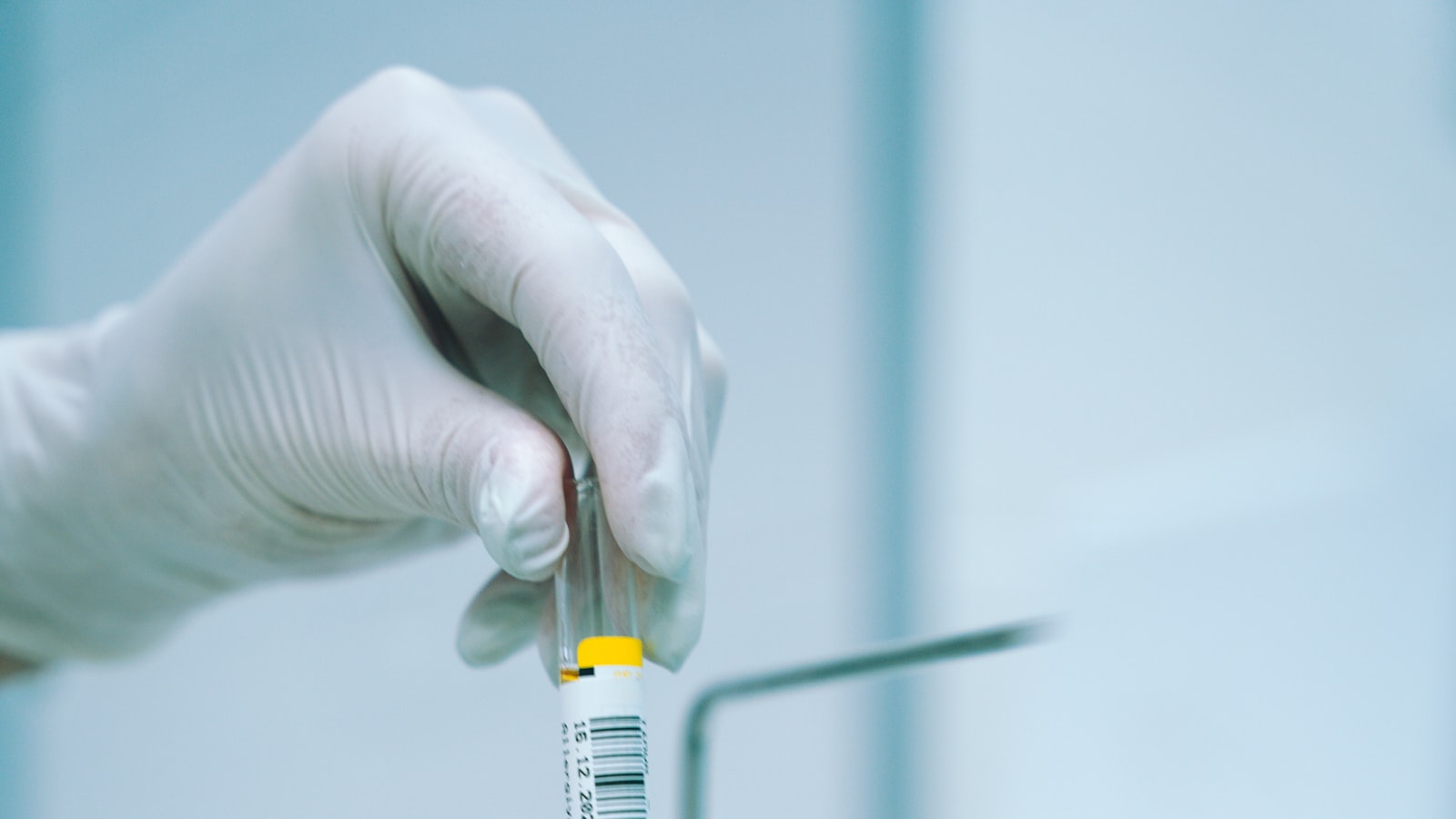 A gloved hand holding a barcoded specimen tube in a clinical laboratory