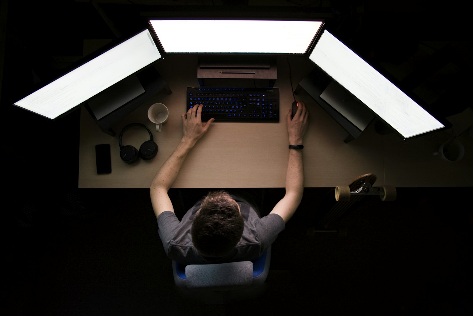 Overhead view of an engineer working across a multi-monitor setup in a darkened room
